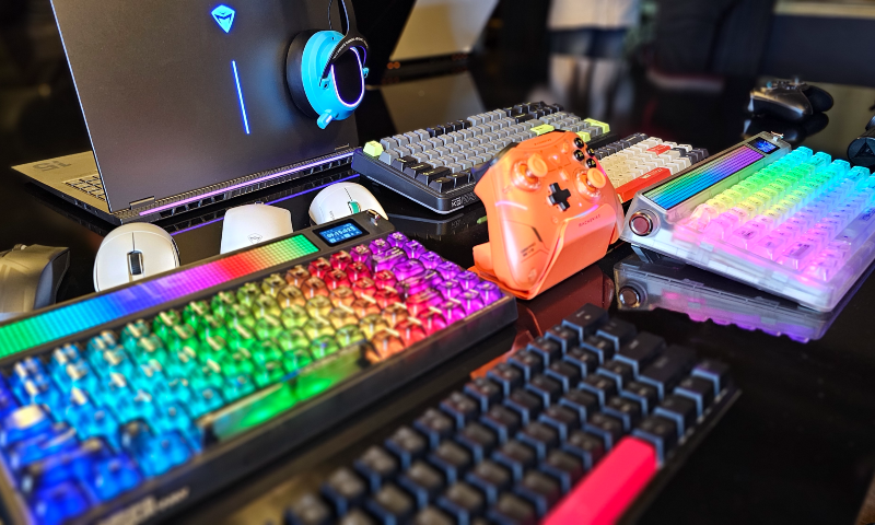 Produtos da Machenike (teclado gamer, controle, mouse, notebook, headset) dispostos sobre uma mesa.